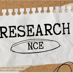 May include: A white piece of paper with the word "RESEARCH" in bold, black letters. Below, the word "NCE" is inside an oval. The paper is taped to a corkboard with brown tape.