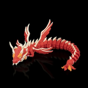 Puede incluir: Una figura de dragón articulada roja y blanca con un diseño detallado. El dragón tiene un cuerpo largo y segmentado, alas y una cabeza detallada con cuernos y dientes afilados. El dragón está posado sobre una superficie negra.