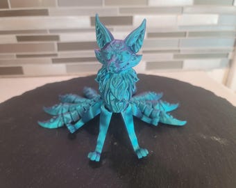 Peut inclure: Une figurine en 3D imprimée en bleu turquoise représentant un kitsune, un renard mythique japonais à plusieurs queues. La figurine présente un design détaillé et texturé et une expression fantaisiste.