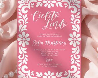 May include: A pink baby shower invitation with white floral border and text. The invitation reads "Cielito Lindo" and includes details for Sofia Martinez's baby shower, including date, time, and location. The invitation is set against a pink fabric background with pearl accents.