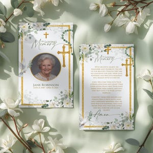 May include: Two rectangular funeral memorial cards featuring white floral borders, gold cross accents, and green eucalyptus leaves. The left card displays a circular portrait of a person with the text In Loving Memory, Jane Robinson, and dates. The right card contains printed prayer text and the word Amen.