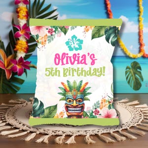 Può includere: Un sacchetto per feste bianco con un bordo superiore verde, con fiori tropicali, foglie e un'illustrazione di maschera tiki. Il testo "Olivia's 5th Birthday!" è visualizzato in rosa e verde.