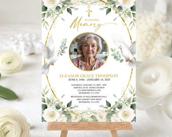 May include: A memorial sign with a photo of a woman, surrounded by white roses, greenery, and doves. The sign reads "In Loving Memory" and includes the name Eleanor Grace Thompson, dates, and service details. The sign is displayed on a small wooden easel.