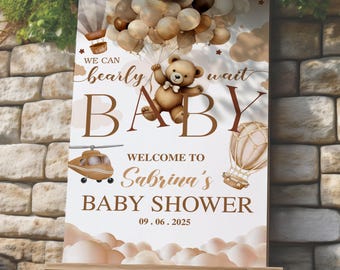 May include: A baby shower sign with a teddy bear holding balloons. The sign reads "We can bearly wait BABY Welcome to Sabrina's BABY SHOWER 09.06.2025". The design includes a helicopter, hot air balloon, and clouds.