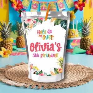 Può includere: Una busta per bevande in plastica trasparente con una cannuccia, con disegni floreali e di foglie tropicali. Il testo recita "Hula on Over Olivia's 5th Birthday!" con lettere colorate. La busta è su un tappetino intrecciato con ananas sullo sfondo.