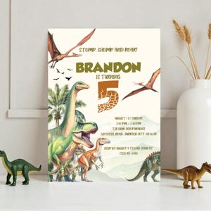 May include: A dinosaur-themed birthday party invitation with a green, brown, and orange color scheme. The invitation features a large number "5" with a dinosaur skin pattern, the words "STOMP, CHOMP AND ROAR!" and "BRANDON IS TURNING 5". The invitation also includes a variety of dinosaurs, including a green Tyrannosaurus Rex, a brown Brachiosaurus, and a green Pterodactyl.