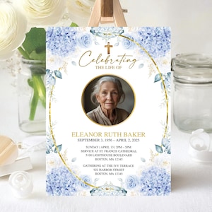 May include: A memorial sign with a photo of a woman, surrounded by a gold frame and floral accents. The sign reads "Celebrating the Life of Eleanor Ruth Baker" with dates and location details. Blue and white flowers decorate the edges.