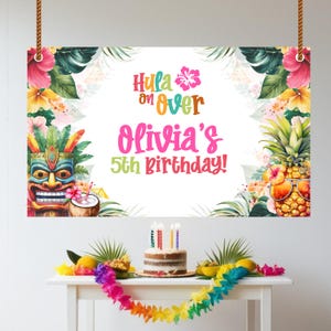 Può includere: Un colorato banner di compleanno con la scritta "Hula on Over Olivia's 5th Birthday!" presenta fiori tropicali, una maschera tiki e un ananas con occhiali da sole. Una torta con candele e una ghirlanda sono su un tavolo sottostante.