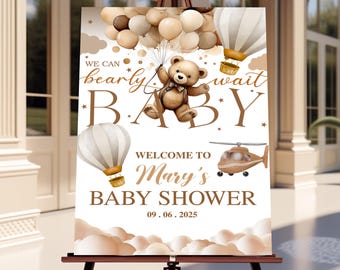 May include: A baby shower welcome sign on a wooden easel. The sign features a teddy bear holding balloons, hot air balloons, and a helicopter. Text reads "We can bearly wait BABY" and "Welcome to Mary's Baby Shower 09.06.2025."