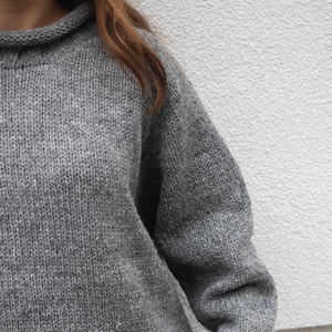 May include: A grey knitted jumper with a high neck and long sleeves.
