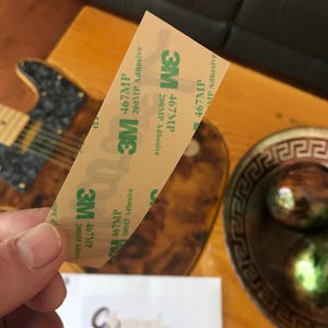 May include: A close-up of a roll of 3M 467MP 200MP Adhesive tape. The tape is beige with green text and a 3M logo.
