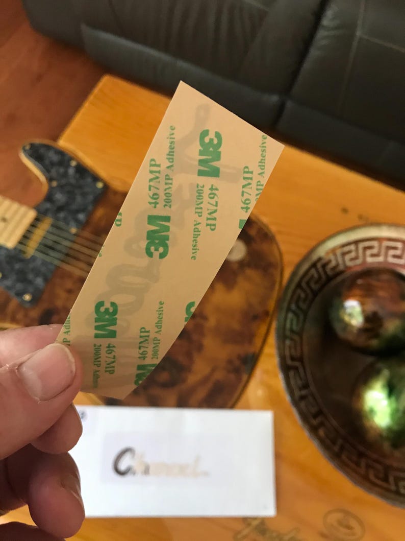 May include: A close-up of a roll of 3M 467MP 200MP Adhesive tape. The tape is beige with green text and a 3M logo.
