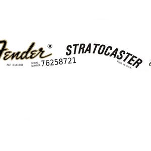 May include: Black and gold Fender Stratocaster guitar decal with the text "Fender", "Stratocaster", "Pat 3,143,028", "Serial Number 76258721", "Made in U.S.A.", and "Original Contour Body Patented".