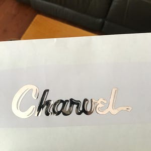 May include: A silver metallic sticker with the word "Charvel" written in a stylized script font.