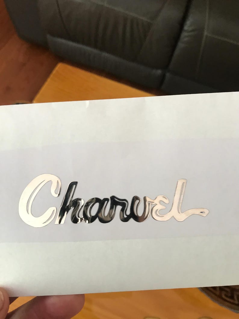 May include: A silver metallic sticker with the word "Charvel" written in a stylized script font.