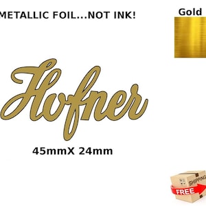 Puede incluir: Logotipo Hofner en lámina dorada, de 45 mm x 24 mm, con el texto "METALLIC FOIL...NOT INK!". La imagen también incluye una muestra de lámina dorada y una pequeña caja con una etiqueta de envío.