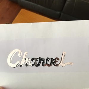 May include: A silver metallic sticker with the word "Charvel" written in a cursive font.