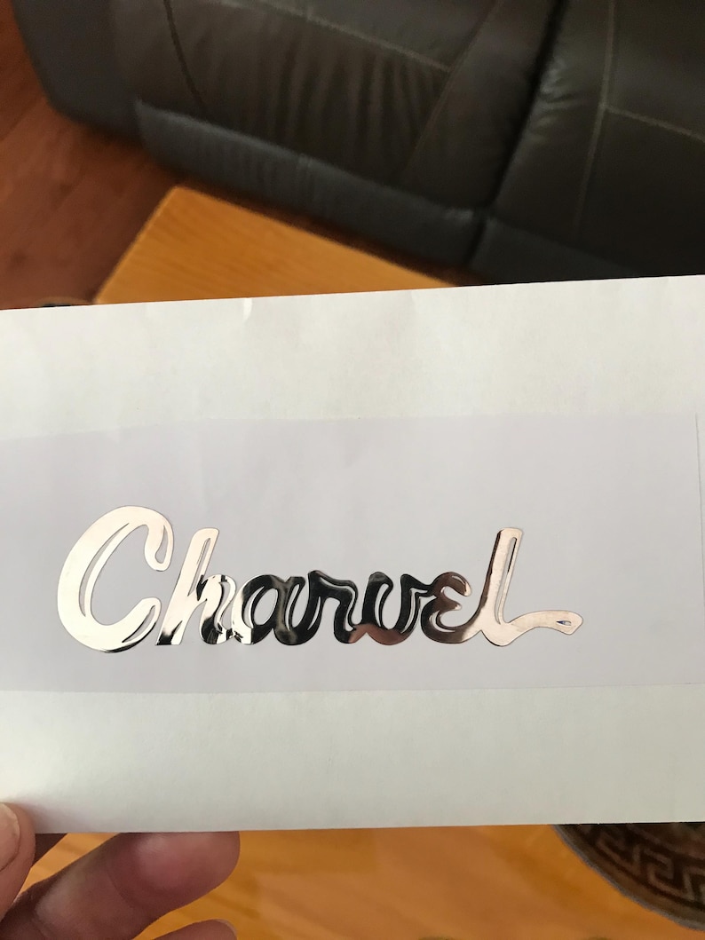 May include: A silver metallic sticker with the word "Charvel" written in a cursive font.