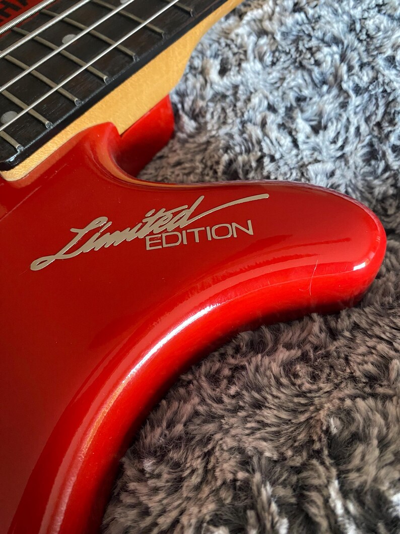 May include: Close-up of a red electric bass guitar with a silver "Limited Edition" inscription on the body.