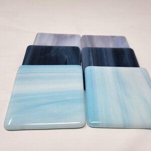 May include: Six square glass coasters in shades of blue and white. The coasters have a marbled or swirled appearance.
