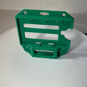 Puede incluir: Un portagafete de plástico verde con dos ranuras para tarjetas. El portagafete tiene un agujero en la parte superior para un cordón o un clip.