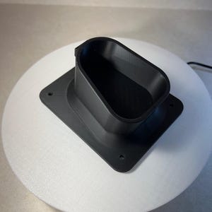 Puede incluir: Un soporte de estación de carga impreso en 3D de plástico negro para un vehículo eléctrico.