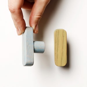 May include: Two wooden cabinet knobs. One is light blue with a cylindrical projection, and the other is a rectangular shape in a light yellow-green color. The knobs are likely for a drawer or cabinet.