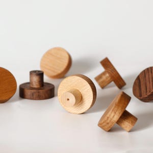Könnte beinhalten: Eine Sammlung von Holzschrankknöpfen in verschiedenen Formen und Holztönen. Die Knöpfe umfassen runde, pilzförmige und T-förmige Designs, die natürliche Holzmaserung und eine helle Oberfläche zeigen. Ideal für Möbel.