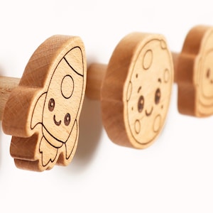 Puede incluir: Tres pomos de madera con tem&aacute;tica espacial. El primero es un cohete, el segundo una luna y el tercero un astronauta. Cada pomo tiene una cara sonriente y est&aacute; hecho de madera de color claro con detalles grabados en negro. Ideal para la habitaci&oacute;n de un ni&ntilde;o.