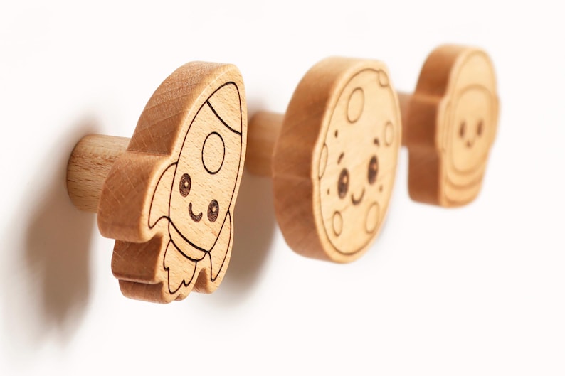Puede incluir: Tres pomos de madera con tem&aacute;tica espacial. El primero es un cohete, el segundo una luna y el tercero un astronauta. Cada pomo tiene una cara sonriente y est&aacute; hecho de madera de color claro con detalles grabados en negro. Ideal para la habitaci&oacute;n de un ni&ntilde;o.