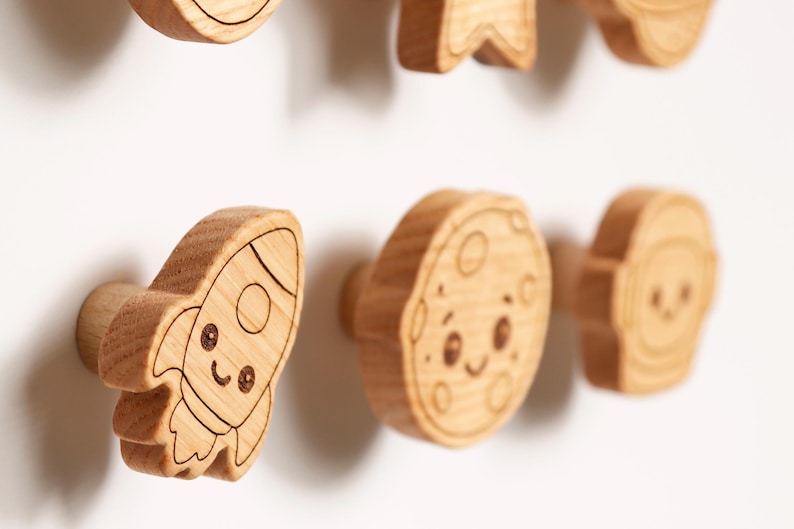 Puede incluir: Pomos de armario de madera con tem&aacute;tica espacial. Los pomos son de color marr&oacute;n claro y presentan dise&ntilde;os grabados de un cohete, una luna y un astronauta con caras sonrientes. Estos pomos decorativos son perfectos para la habitaci&oacute;n de un ni&ntilde;o.