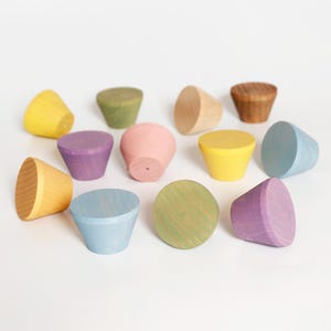 Könnte beinhalten: Eine Sammlung farbenfroher Holzknöpfe in verschiedenen Farbtönen, darunter Gelb, Lila, Rosa und Blau. Die Knöpfe haben eine konische Form mit flacher Oberseite und liegen auf einer weißen Oberfläche. Maße in cm.