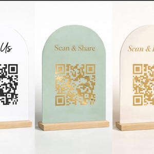 Puede incluir: Tres letreros arqueados con códigos QR. Un letrero es blanco con el texto "Tag Us" en negro. El segundo letrero es verde menta con "Scan & Share" en dorado. El tercer letrero es blanquecino con "Scan & Indulge" en dorado.