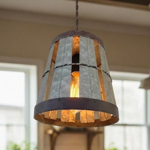 May include: A rustic kitchen scene with a wooden table set for breakfast. A steaming mug and croissant sit on the table. A metal and wood pendant light hangs above. Family members are in the background.