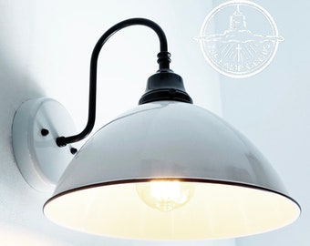 May include: White enamel wall sconce with a black metal arm and a white shade. The light is on and the bulb is visible.