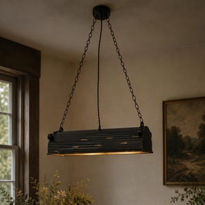 May include: A rectangular pendant light fixture with a distressed black finish and gold-toned accents. The fixture is suspended by two thin metal chains attached to a central canopy and features a horizontal, ribbed metal housing design.