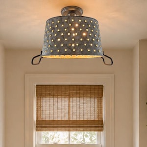 May include: A ceiling-mounted light fixture featuring a cylindrical, galvanized metal shade with a perforated pattern that allows light to pass through. The fixture has a dark metal frame with two curved handles on the sides and a central mount.
