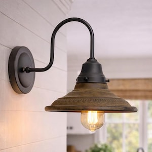 May include: A rustic-style wall-mounted light fixture with a distressed brown shade and a black curved arm. The light has a vintage Edison bulb. The fixture is mounted on a white wall.