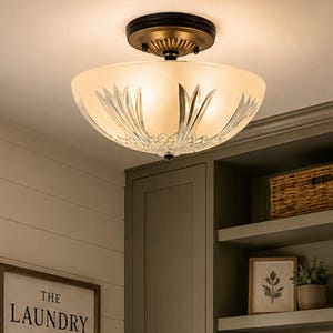May include: A semi-flush mount ceiling light with a frosted glass bowl shade featuring etched leaf patterns, suspended by a dark bronze metal fixture. The light is illuminated, casting a warm glow in a laundry room with sage green cabinets.