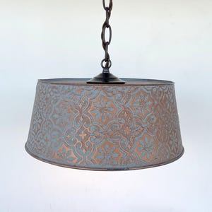 Puede incluir: Una l&aacute;mpara colgante con una pantalla estampada. La pantalla es de color azul verdoso apagado con un dise&ntilde;o floral color cobre. La l&aacute;mpara cuelga de una cadena marr&oacute;n oscuro y tiene una base negra.