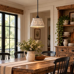 May include: A galvanized metal pendant light fixture with a flared shade featuring cut-out star patterns. The light hangs from a black cord and illuminates a dining area with a wooden table, black chairs, and a white ceramic pitcher with flowers.
