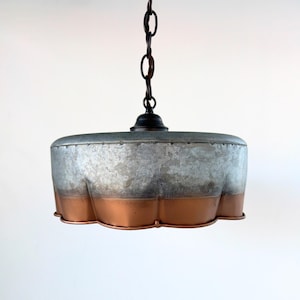 May include: A hanging pendant light with a galvanized metal shade and a copper-colored bottom edge. The light fixture is suspended from a dark chain and has a black fixture cap. The shade has a unique, scalloped edge.