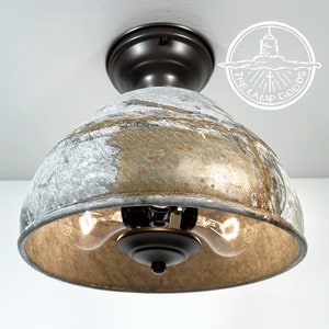 May include: A two-light ceiling fixture with a distressed metal shade in shades of gray, gold, and brown. The fixture has a black metal base and is designed in a farmhouse style.