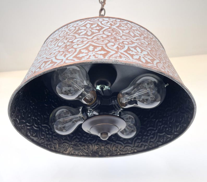 Puede incluir: Una l&aacute;mpara colgante r&uacute;stica con una pantalla estampada de color cobre y un interior negro. La l&aacute;mpara tiene cinco bombillas Edison de estilo vintage. La pantalla est&aacute; suspendida de una cadena.