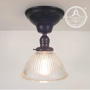 May include: A black ceiling light fixture with a clear glass shade. The shade has vertical ribs and a rounded shape. The fixture is attached to a white ceiling.