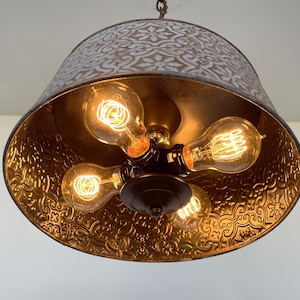 Puede incluir: Una l&aacute;mpara colgante r&uacute;stica con una pantalla de metal con un patr&oacute;n floral. El interior es dorado y alberga cinco bombillas de estilo Edison. La l&aacute;mpara cuelga de una cadena.