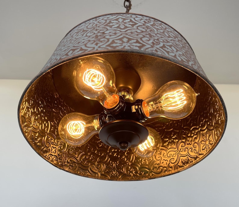 Puede incluir: Una l&aacute;mpara colgante r&uacute;stica con una pantalla de metal con un patr&oacute;n floral. El interior es dorado y alberga cinco bombillas de estilo Edison. La l&aacute;mpara cuelga de una cadena.