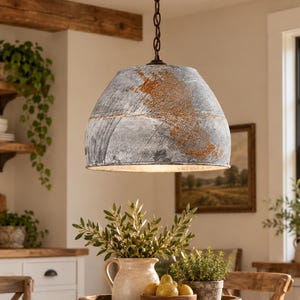 May include: A dome-shaped pendant light fixture with a distressed galvanized metal finish featuring patches of rust-colored oxidation. The lamp hangs from a dark metal chain and has a wide, open bottom that directs light downward.