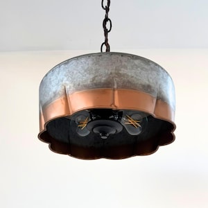 May include: A hanging pendant light with a galvanized metal shade and copper-colored band. The light fixture has a scalloped edge and three visible light bulbs. The fixture hangs from a dark chain.