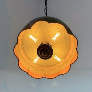 May include: A unique, hanging light fixture with a scalloped, flower-like shade. The shade is a warm, golden color with a dark, metallic rim. Four Edison-style light bulbs are visible inside the shade, creating a warm glow. The fixture hangs from a dark chain.
